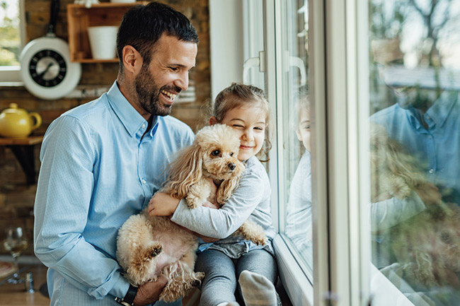Father and daughter smiling hugging a dog