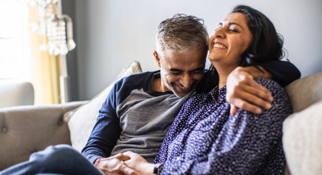 Mature couple holding hands and laughinig on couch